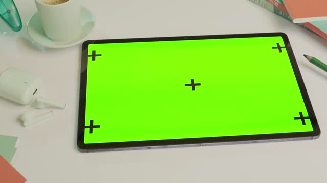 A sleek tablet featuring a green screen device sits on a desk surrounded by various office items.