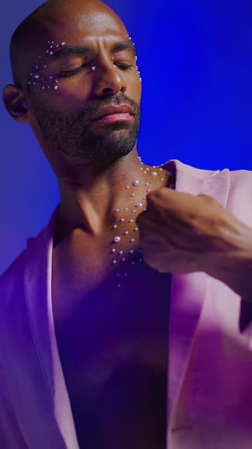Man in stylish lighting with decorative gems on chest.