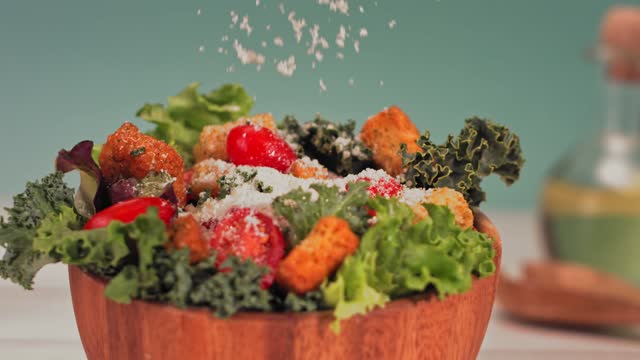 Parmesan cheese sprinkled in slow motion over a green delicious salad .