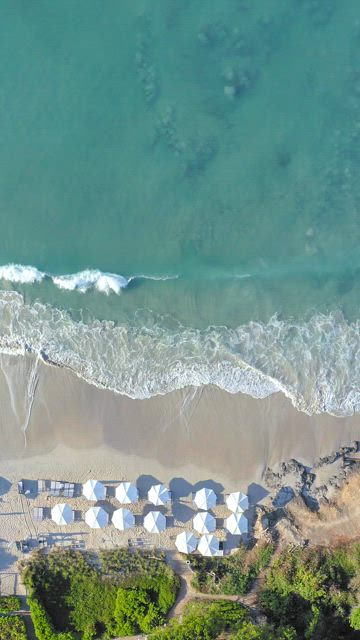 Aerial view of the beautiful turquoise  waves crashing on the sand beach with white umbrellas .
