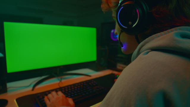 A young gamer in front of a pc monitor with a green screen and an RGB PC rig.