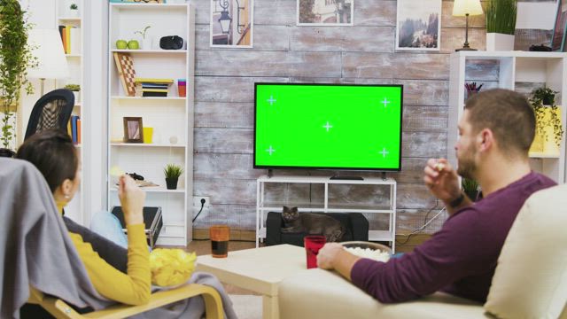 Couple watching green screen TV and eating popcorn.